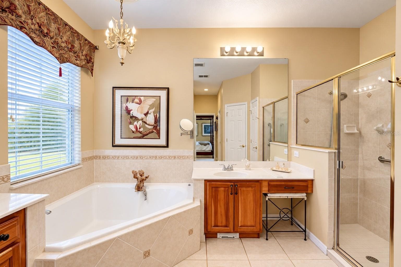 SPACIOUS AND ELEGANT PRIMARY BATHROOM FEATURING SOARING CEILINGS, A RELAXING OVERSIZED SOAKING TUB, AND A SEPARATE WALK-IN SHOWER WITH BEAUTIFUL CUSTOM TILEWORK AND GLASS ENCLOSURE! Enjoy DUAL VANITIES WITH BEAUTIFUL WOOD CABINETRY, GENEROUS COUNTER SPACE, AND ABUNDANT STORAGE! A large window fills the space with natural light, while elegant lighting and decorative tile accents add warmth and charm. THE PERFECT PRIVATE RETREAT TO RELAX AND UNWIND AFTER A LONG DAY! - 14542 RIVIERA POINTE DR, ORLANDO