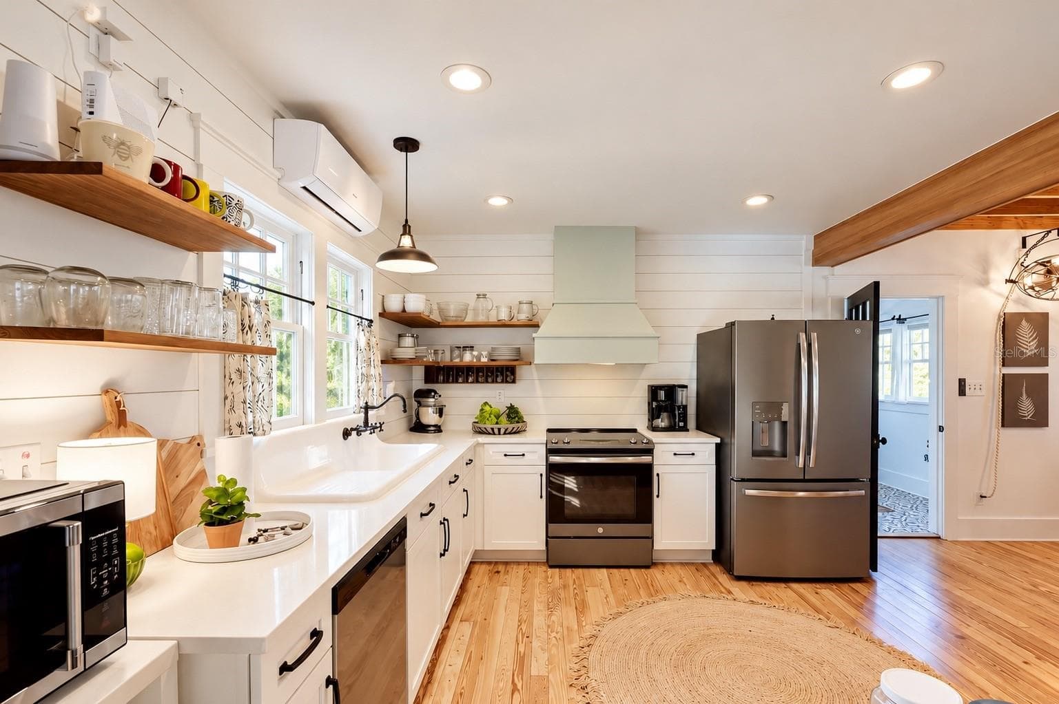 Updated FARMHOUSE-STYLE KITCHEN featuring white cabinetry, shiplap walls, gorgeous wood flooring, floating wood shelves, a charming OVERSIZED FARMHOUSE APRON-FRONT SINK beneath sun-filled windows, stainless steel appliances, and a stylish range hood! - 1901 10TH ST, ST CLOUD