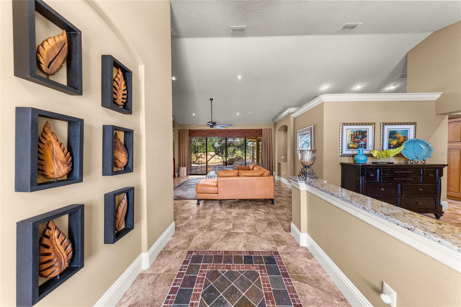 Welcoming foyer featuring decorative tile flooring, high ceilings, elegant crown molding, and an open view into the spacious living area with sliding glass doors overlooking the screened outdoor retreat. - 6501 SW 179TH AVENUE RD, DUNNELLON