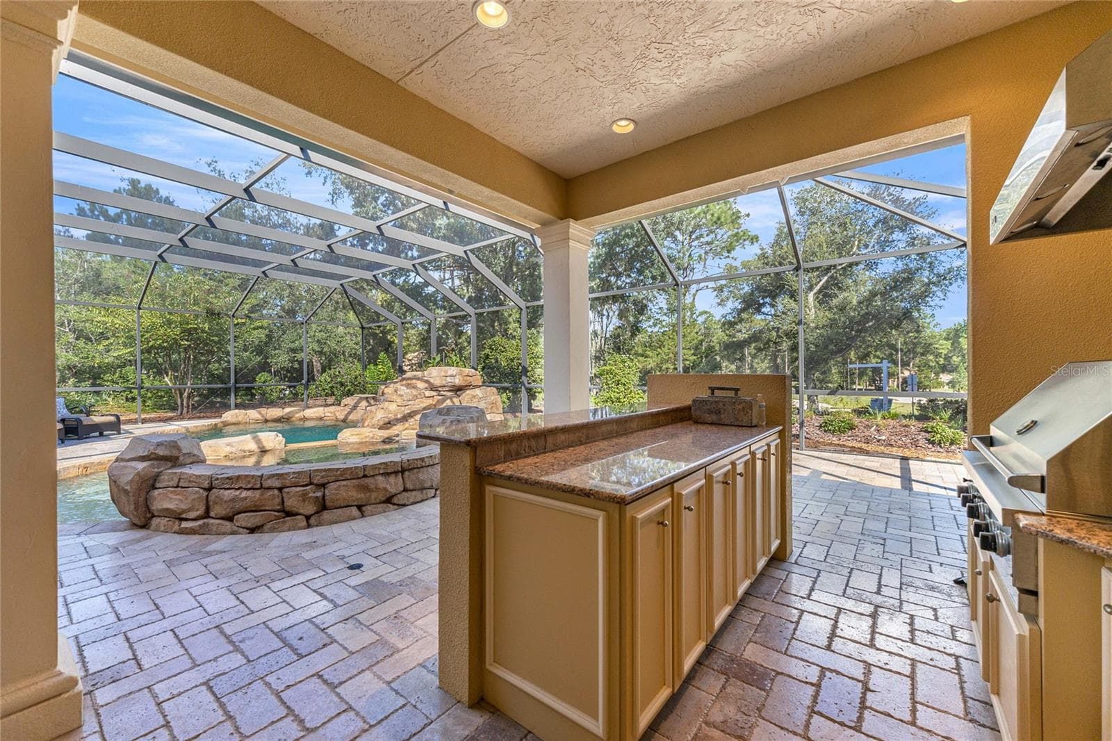 Impressive summer kitchen with built-in grill, granite countertops, sink, cabinetry, and poolside entertaining space. - 6501 SW 179TH AVENUE RD, DUNNELLON