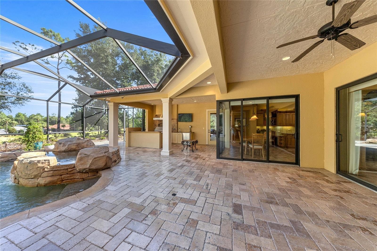 Expansive covered lanai with brick pavers, ceiling fan, and views of the custom pool and spa. - 6501 SW 179TH AVENUE RD, DUNNELLON