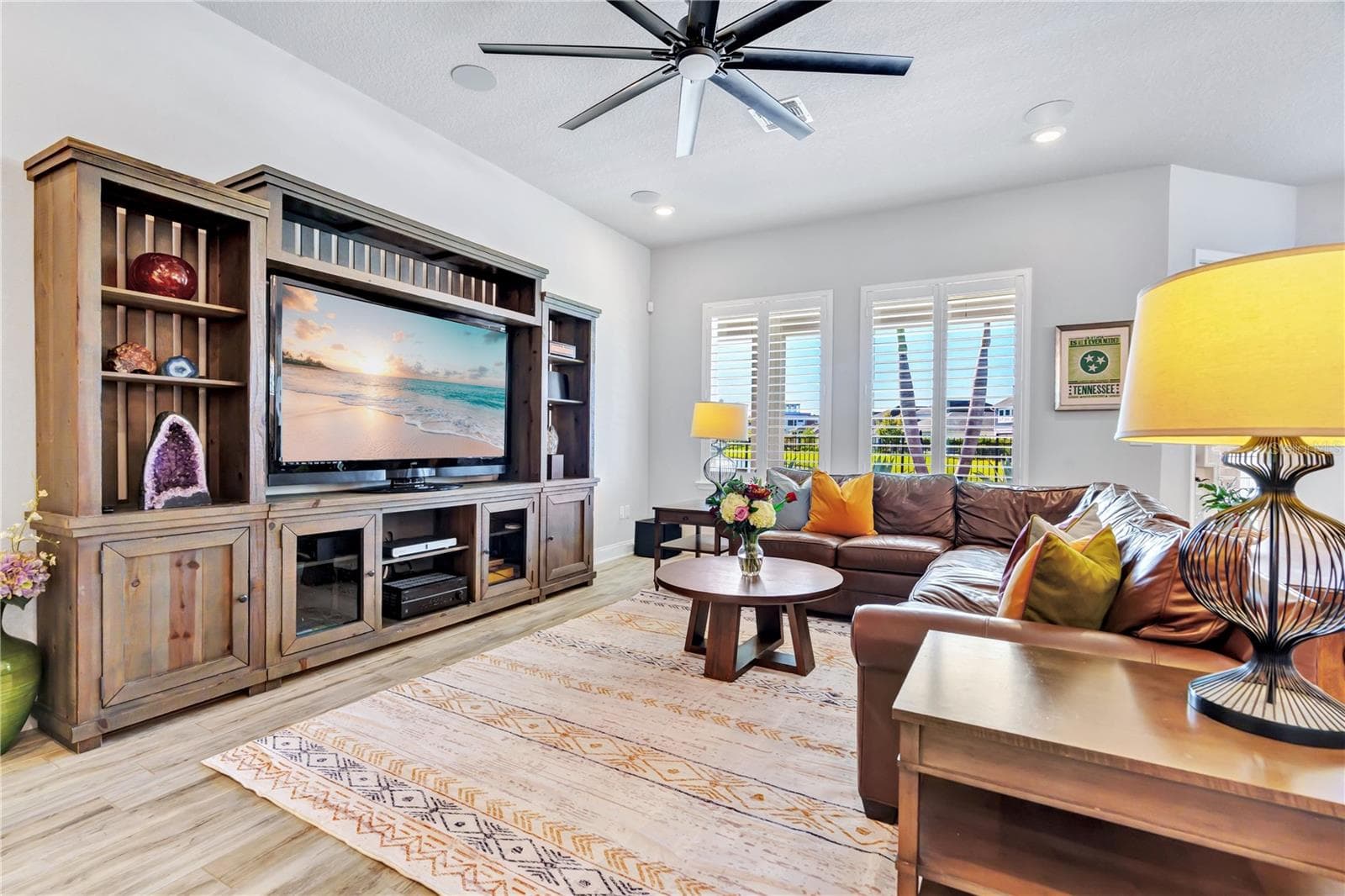 Spacious family room with a custom entertainment wall and wood look plank tile, flowing into the kitchen and dining area. - 8336 CANETTI ST, ORLANDO