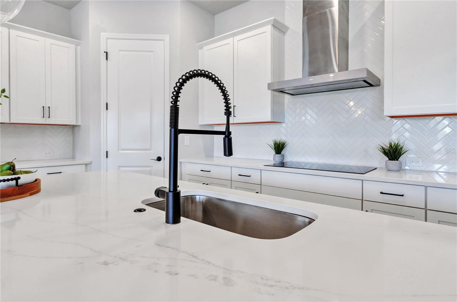 Quartz counters, undermount sink, matte black faucet, and herringbone tile backsplash with a view into the home. - 8336 CANETTI ST, ORLANDO