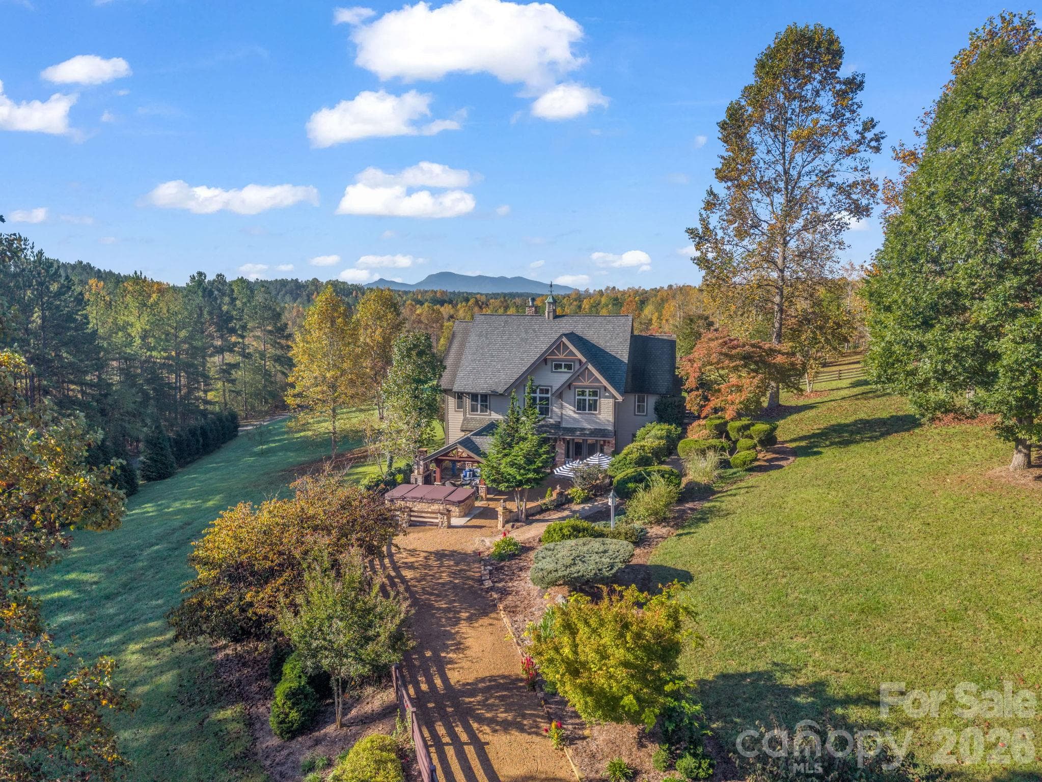 Aerial showcasing the mountain views, privacy, over $200K in added landscaping, swim spa, pavilion with Italian inspired ambiance and 8+ acres of cleared pasture and fencing added - 140 Blazing Star Lane, Mill Spring