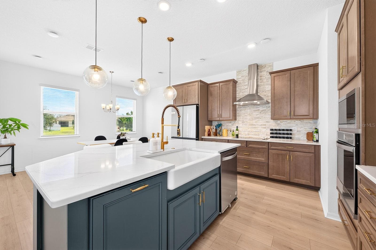 A beautiful BELFAST SINK, built-in oven, sleek cooktop with a CONTEMPORARY RANGE HOOD, and a spacious center island with breakfast bar seating complete this thoughtfully designed space. - 1785 PETIOLE PL, KISSIMMEE