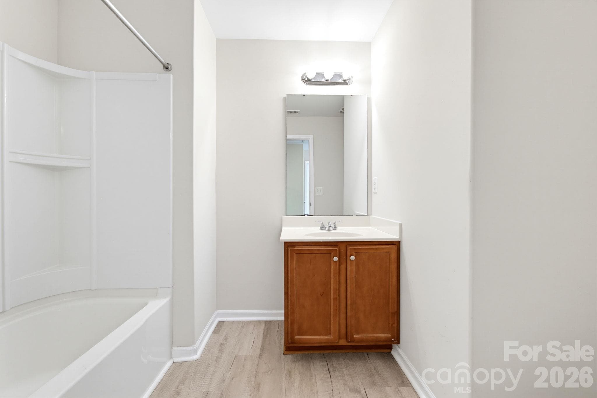 Full bathroom with a wood vanity, bright lighting, and a tub and shower combination. - 5718 Natick Drive, Charlotte