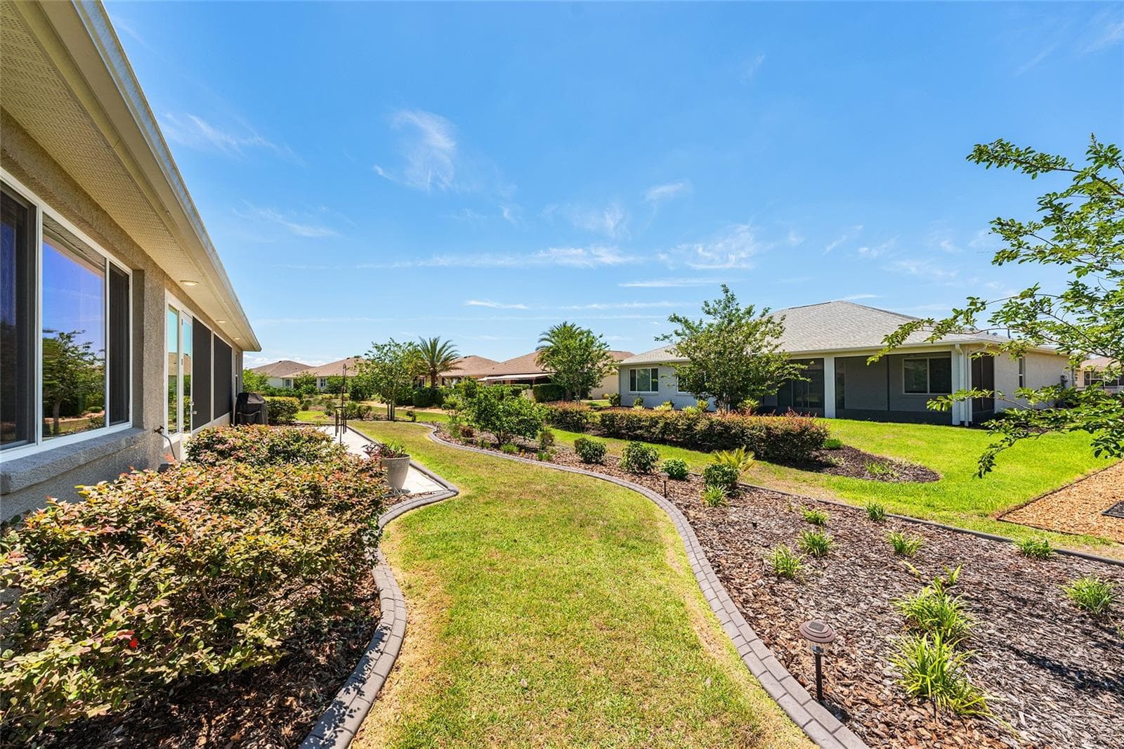 Beautifully landscaped backyard featuring attractive concrete curbing, established shrubs, colorful plantings, and a lush green lawn. Thoughtfully designed landscape beds enhance the outdoor setting and create an inviting space to enjoy Florida living. - 8290 SW 92ND CIR, OCALA