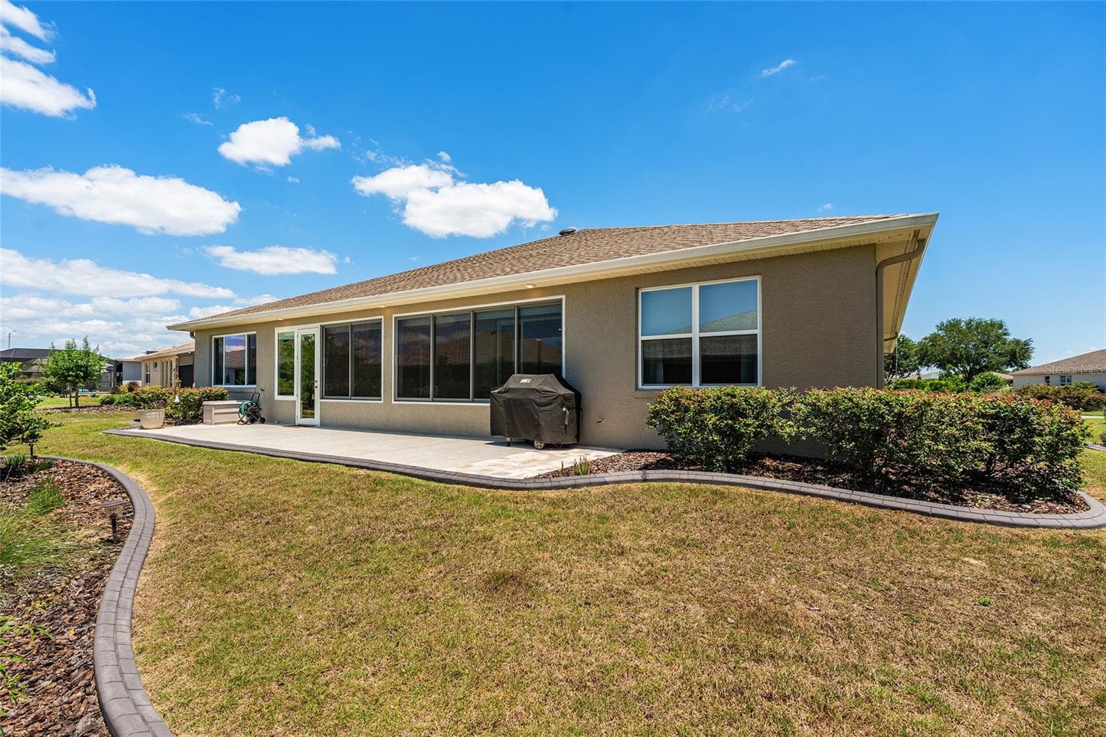Full rear view of the home showcasing the expansive patio, enclosed lanai, and beautifully maintained landscaping. The generous backyard provides plenty of open space to relax and enjoy the Florida lifestyle. - 8290 SW 92ND CIR, OCALA