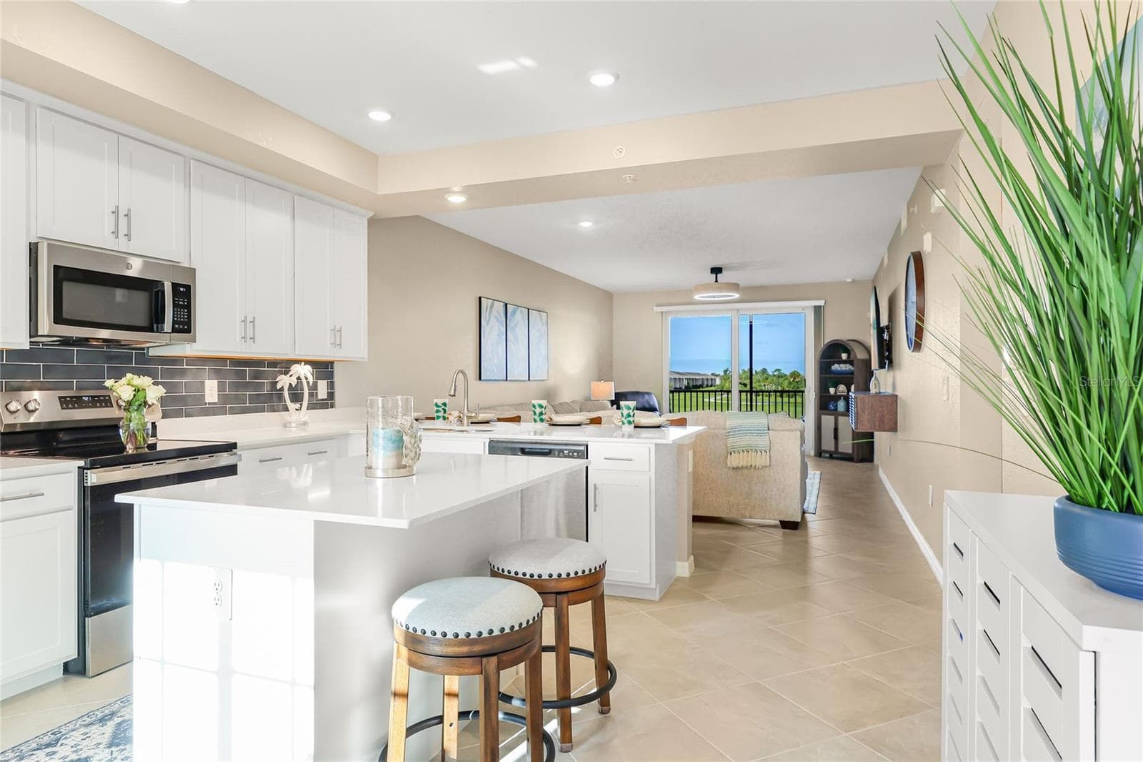 Open floor plan featuring a spacious kitchen with abundant counter space for meal preparation and ample seating, ideal for cooking and entertaining, all overlooking the living area with beautiful golf course, water, and preserve views. - 17565 OPAL SAND DR #204, VENICE