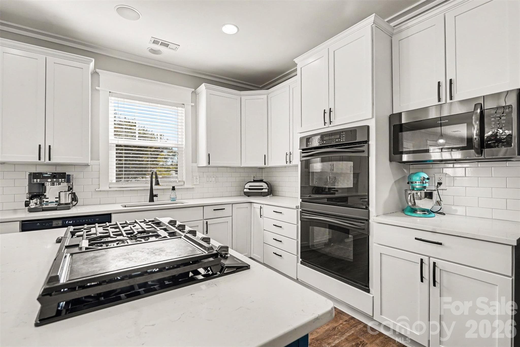 Love the sleek design of this kitchen. White cabinets, white subway tile backsplash, built-in double ovens, built-in Gas cooktop. Love the window above the sink! - 3585 Leighton Drive SW, Concord