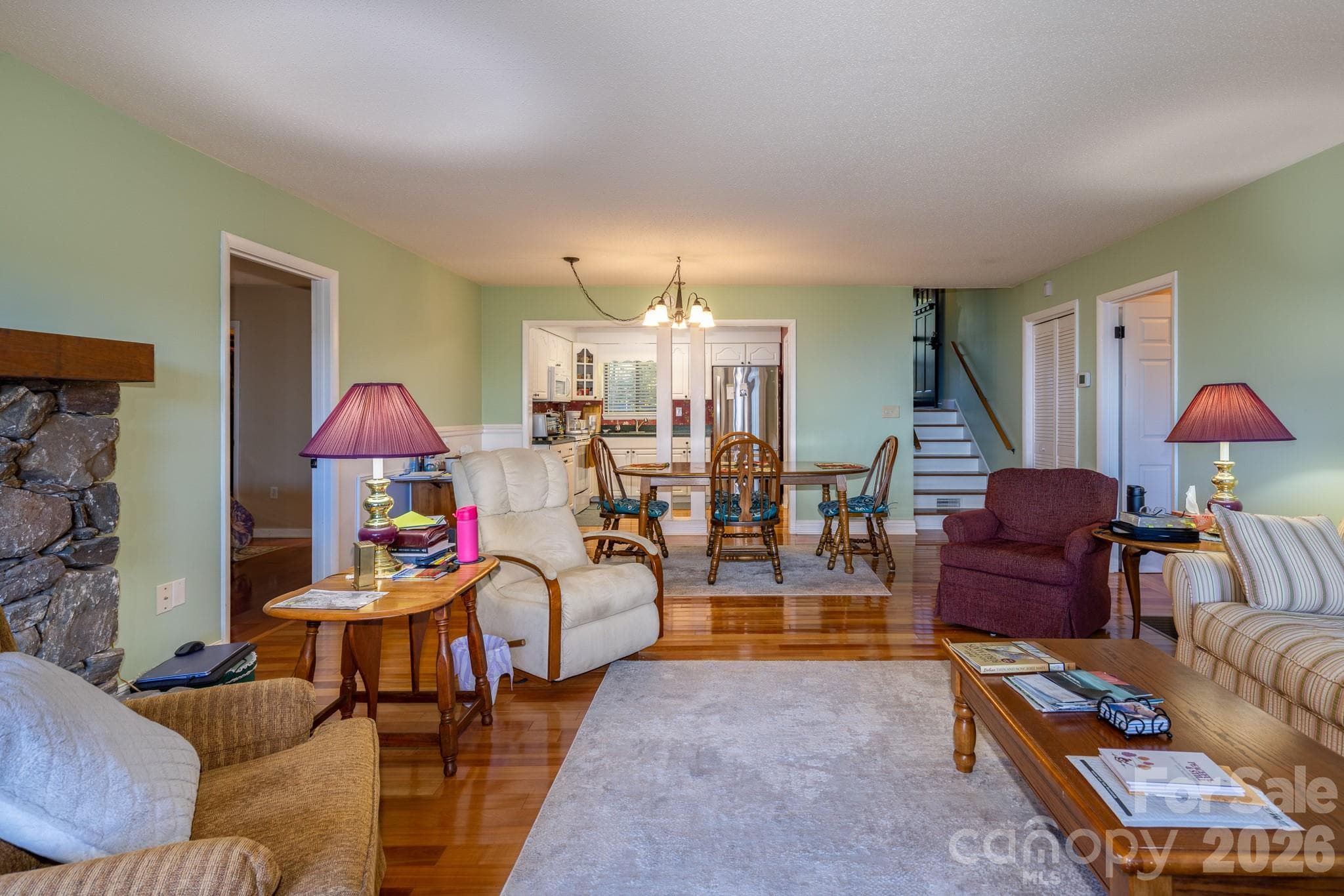 Another view of the inviting living and dining areas, highlighting hardwood flooring, a stone fireplace, and convenient kitchen access. - 524 Three Mile Knob Road, Pisgah Forest