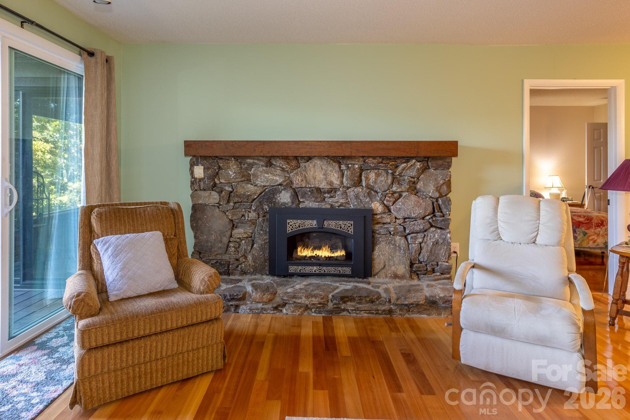 Native stone fireplace with handsome solid wood mantel, gas fireplace insert, and raised stone hearth. A beautiful focal point that adds warmth and mountain character to the living room. - 524 Three Mile Knob Road, Pisgah Forest