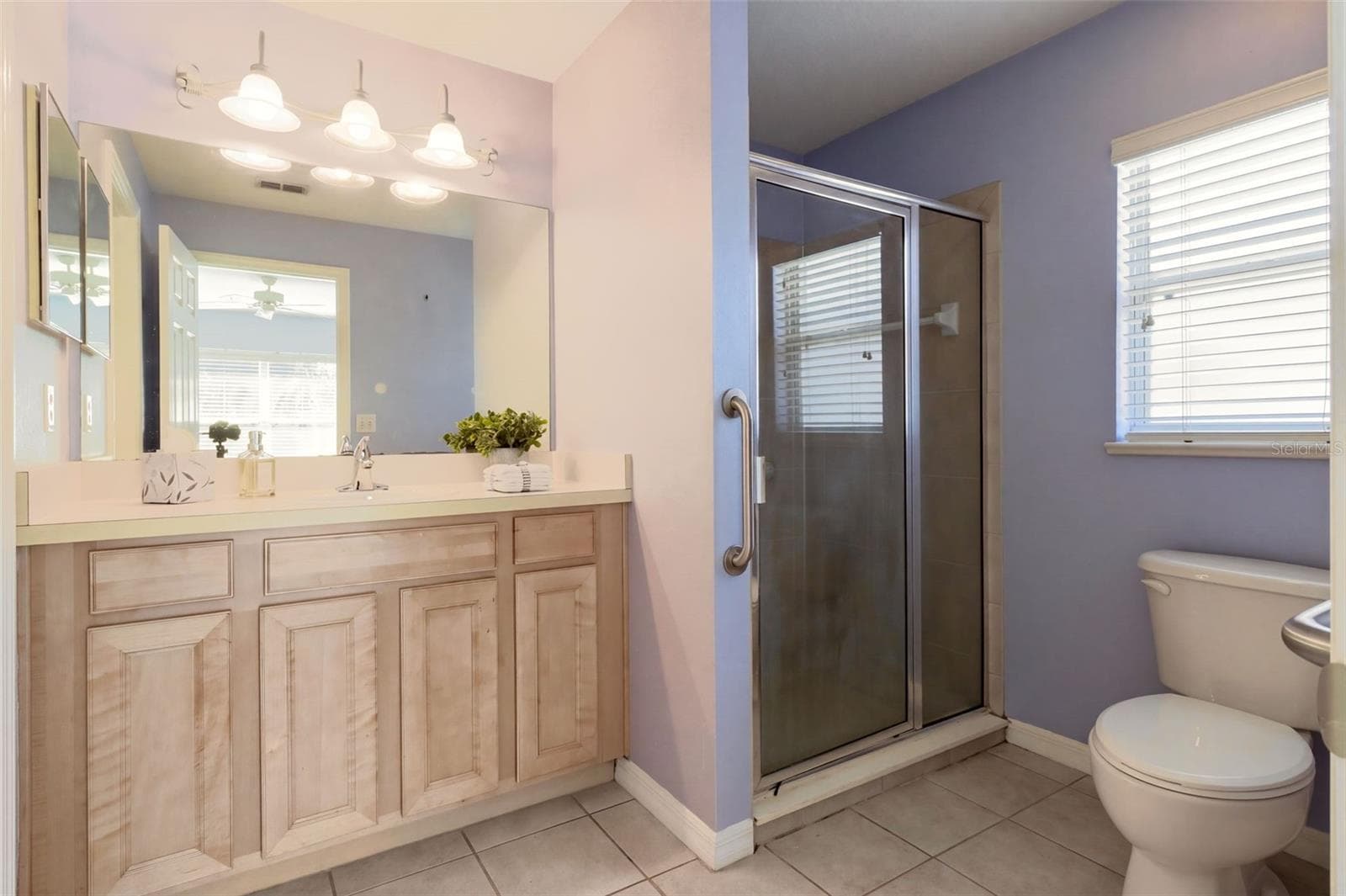 The en-suite primary bathroom is designed for comfort, featuring a comfort-height vanity, tile flooring, and a walk-in shower with a glass door. - 3437 GRENVILLE DR, WINTER HAVEN