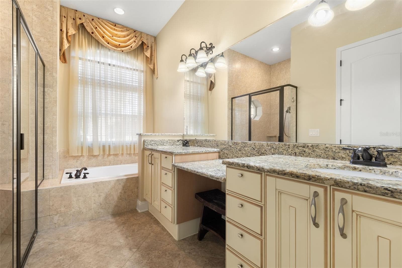 An Italian-inspired primary bathroom featuring dual vanities with granite countertops, a dedicated makeup area, soaking tub, and separate tiled shower. - 25 EMERALD LAKE CT, PALM COAST
