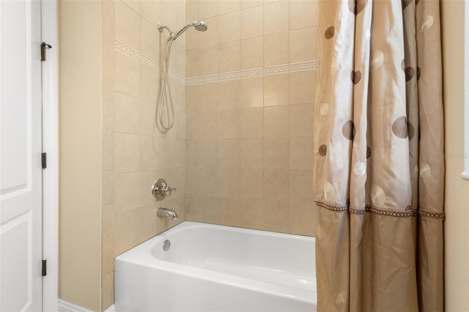 A closer look at the first-floor guest bathroom's tub/shower combination, featuring decorative tile accents and a handheld showerhead. - 25 EMERALD LAKE CT, PALM COAST